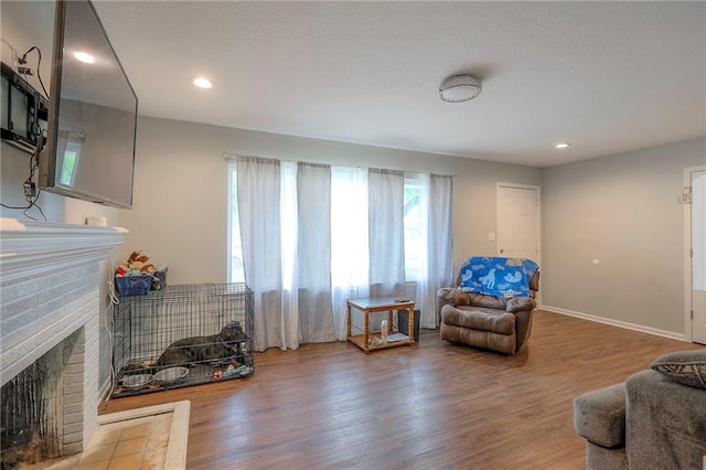 living area with a brick fireplace, recessed lighting, baseboards, and wood finished floors
