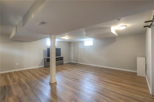 below grade area with baseboards, wood finished floors, and visible vents