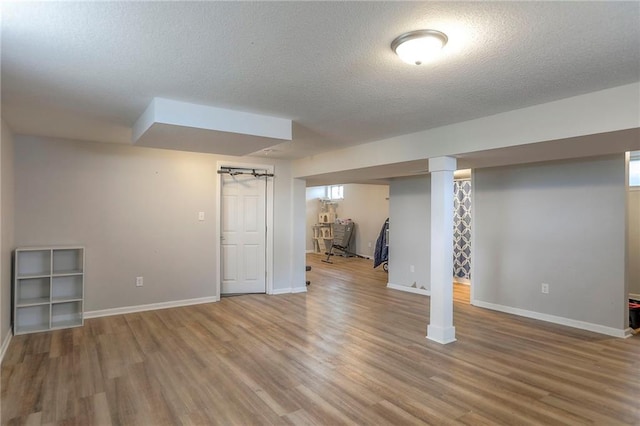 finished below grade area featuring baseboards, a textured ceiling, and wood finished floors