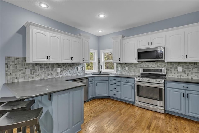 kitchen featuring a kitchen bar, appliances with stainless steel finishes, a sink, a peninsula, and white cabinetry