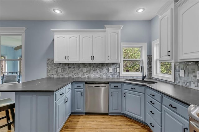 kitchen featuring a sink, a peninsula, dishwasher, and dark countertops