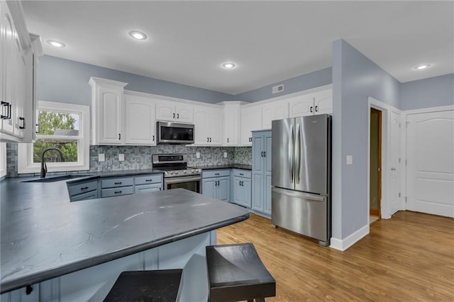 kitchen featuring a peninsula, dark countertops, white cabinets, a sink, and appliances with stainless steel finishes