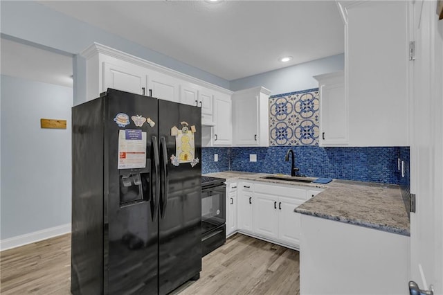 kitchen featuring decorative backsplash, white cabinets, a sink, light wood-style flooring, and black appliances