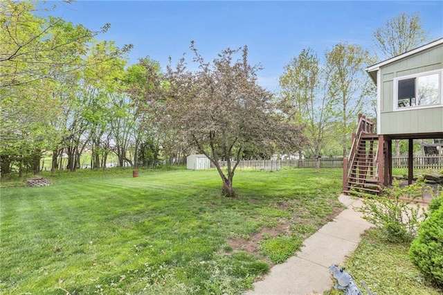 view of yard with fence, a storage unit, a wooden deck, stairway, and an outbuilding