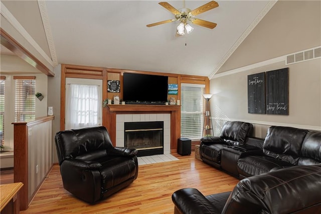 living area featuring ceiling fan, visible vents, a tiled fireplace, wood finished floors, and lofted ceiling