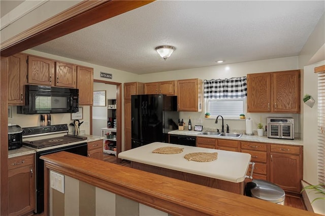 kitchen featuring a sink, light countertops, a textured ceiling, a center island, and black appliances