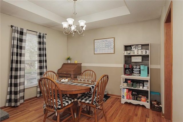 dining room featuring an inviting chandelier, light wood-style flooring, baseboards, and a tray ceiling