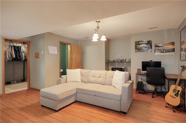 living room with visible vents, a textured ceiling, light wood finished floors, and an inviting chandelier