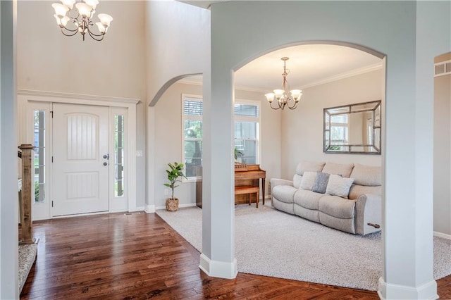 foyer with crown molding, arched walkways, wood finished floors, baseboards, and a notable chandelier