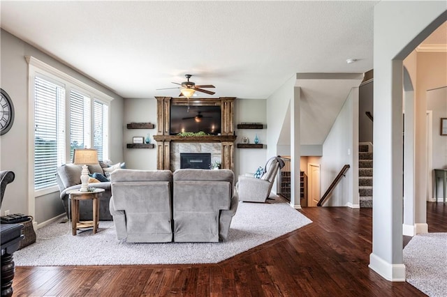 living room featuring ceiling fan, wood finished floors, stairway, baseboards, and a glass covered fireplace