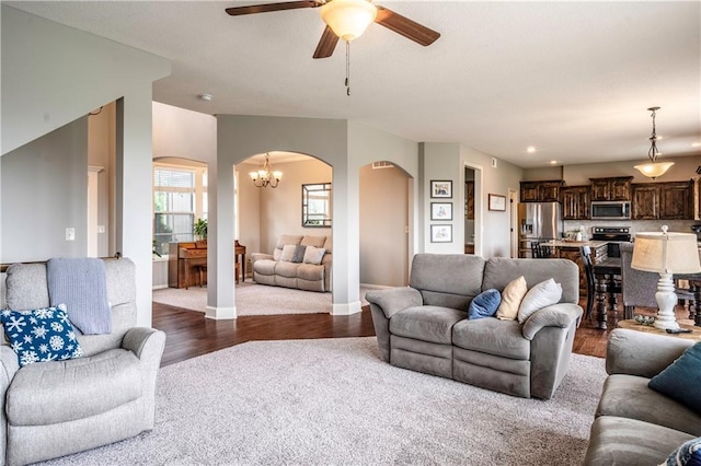 living room featuring arched walkways, baseboards, ceiling fan with notable chandelier, and dark wood-type flooring