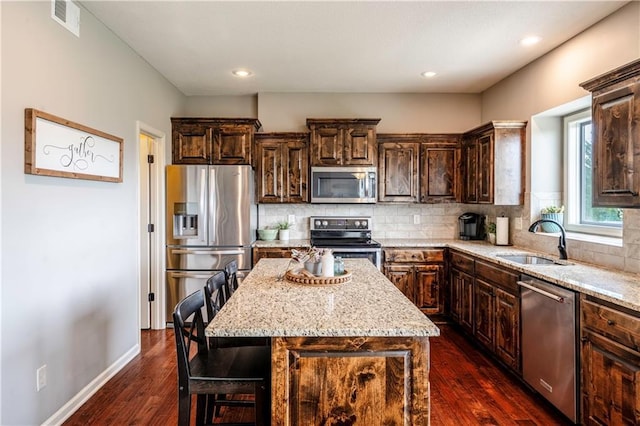 kitchen with dark brown cabinetry, dark wood-style floors, light stone counters, a sink, and stainless steel appliances