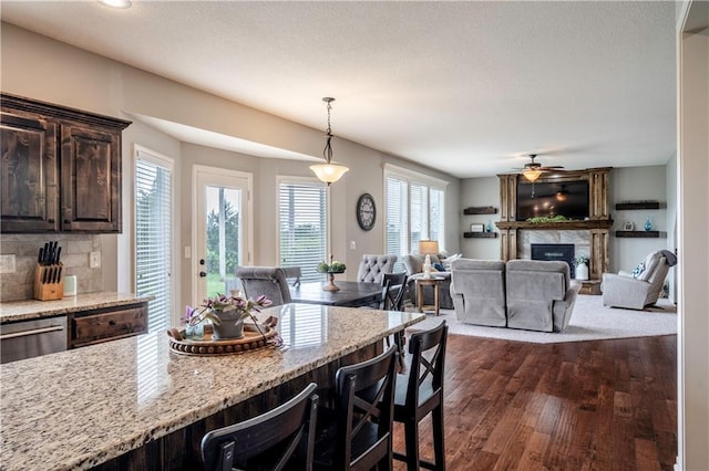 kitchen featuring dark brown cabinets, light stone countertops, hanging light fixtures, a kitchen breakfast bar, and dark wood finished floors