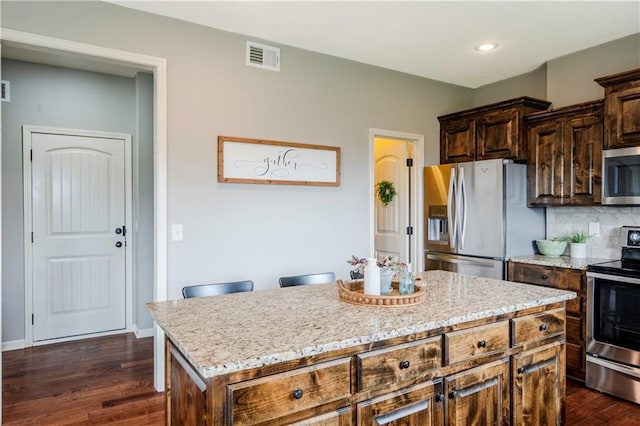 kitchen with visible vents, dark wood-style flooring, light stone countertops, a center island, and stainless steel appliances