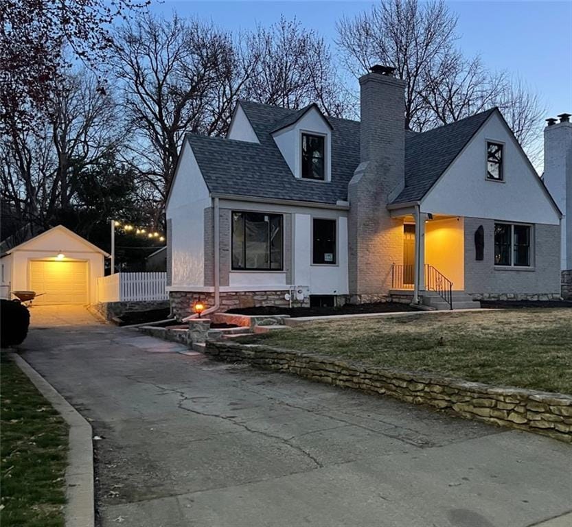 cape cod home featuring a chimney, an outdoor structure, aphalt driveway, a detached garage, and a front lawn