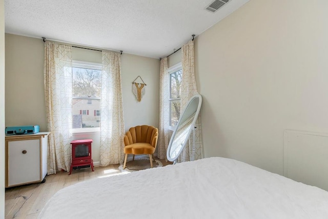 bedroom with wood finished floors, visible vents, a textured ceiling, and a wood stove