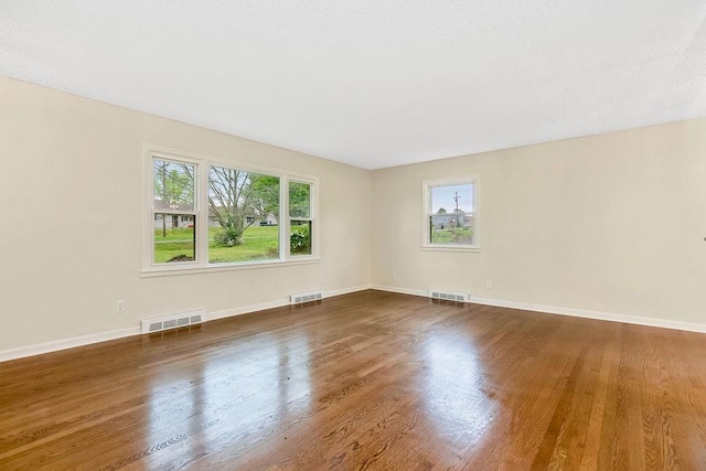 unfurnished room with baseboards, wood finished floors, and visible vents