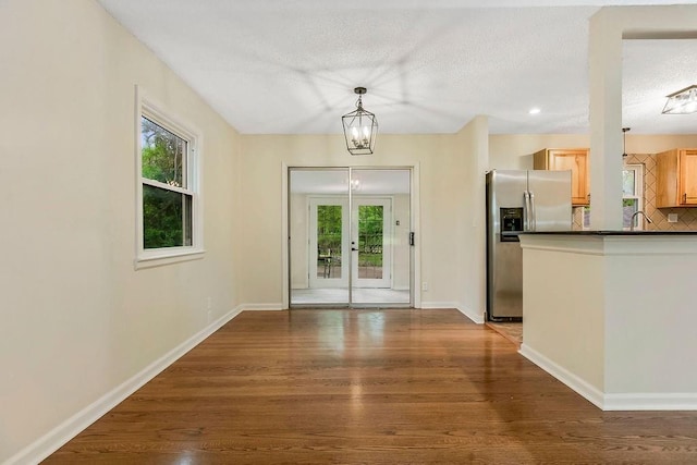 unfurnished dining area with french doors, a textured ceiling, baseboards, and wood finished floors