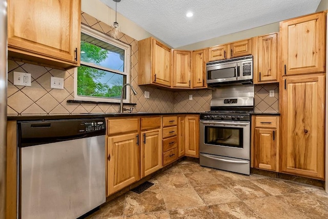 kitchen featuring stone finish floor, backsplash, a textured ceiling, dark countertops, and stainless steel appliances