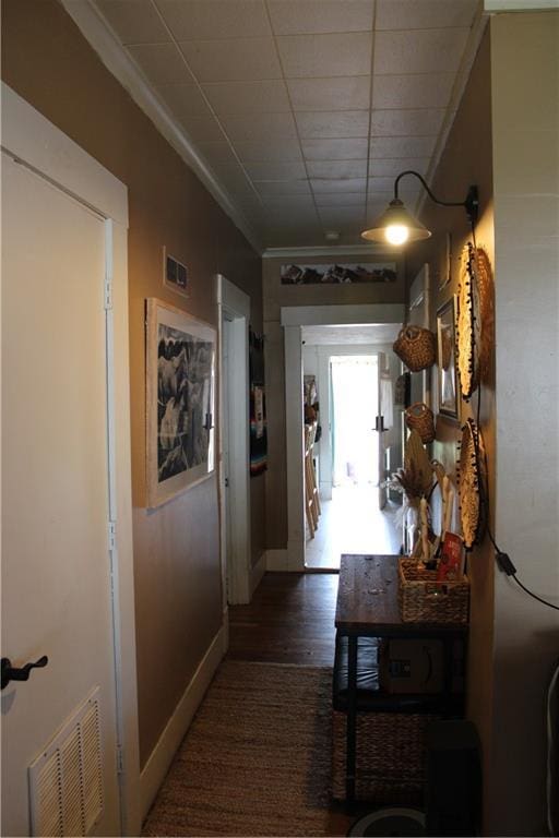 corridor with baseboards, ornamental molding, visible vents, and wood finished floors