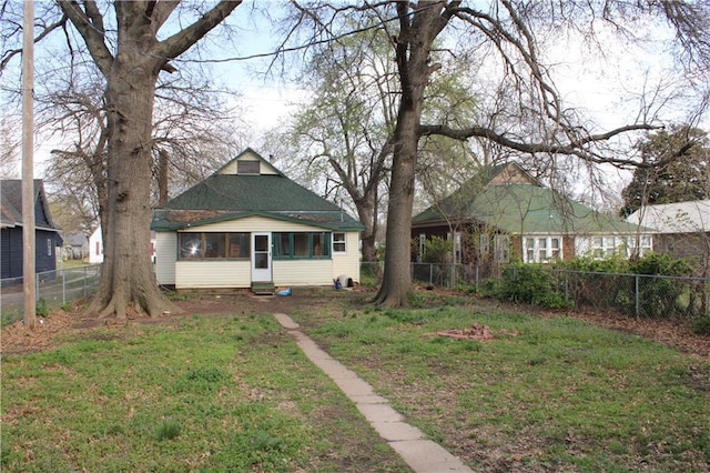 back of property with a fenced backyard, a lawn, a shingled roof, and a sunroom