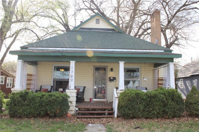 view of front of property with covered porch, roof with shingles, and a chimney