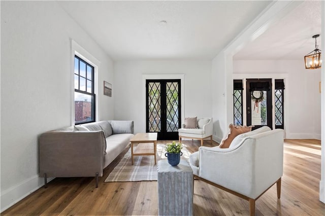 living area featuring baseboards, a notable chandelier, french doors, and wood finished floors
