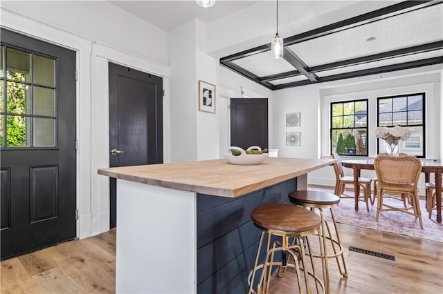 kitchen with light wood-style floors, wooden counters, a breakfast bar area, and coffered ceiling