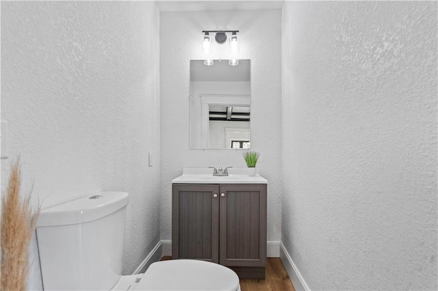 bathroom featuring toilet, a textured wall, wood finished floors, and baseboards