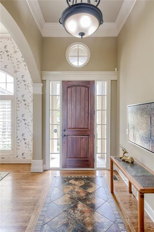 foyer entrance featuring arched walkways, ornamental molding, and baseboards