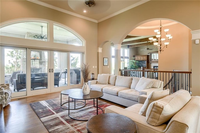 living area featuring arched walkways, decorative columns, ceiling fan with notable chandelier, and wood finished floors