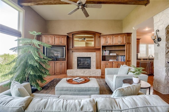 living room with a ceiling fan, beamed ceiling, a glass covered fireplace, and wood finished floors