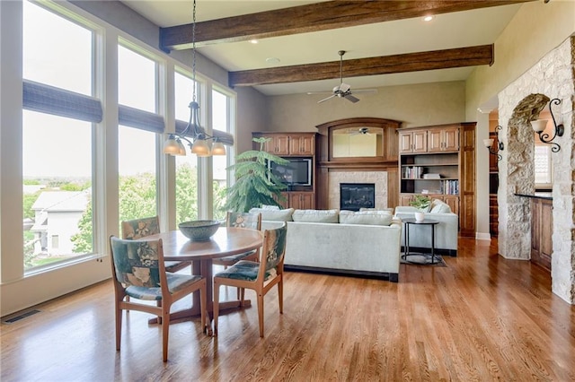 interior space featuring visible vents, beamed ceiling, ceiling fan with notable chandelier, light wood finished floors, and a glass covered fireplace