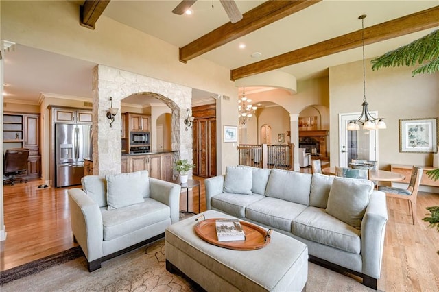 living room featuring beam ceiling, light wood-type flooring, recessed lighting, arched walkways, and ceiling fan with notable chandelier