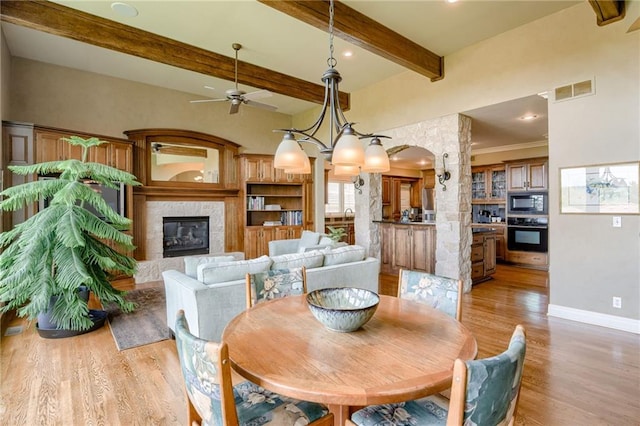 dining room featuring ceiling fan, beam ceiling, light wood finished floors, a fireplace, and baseboards