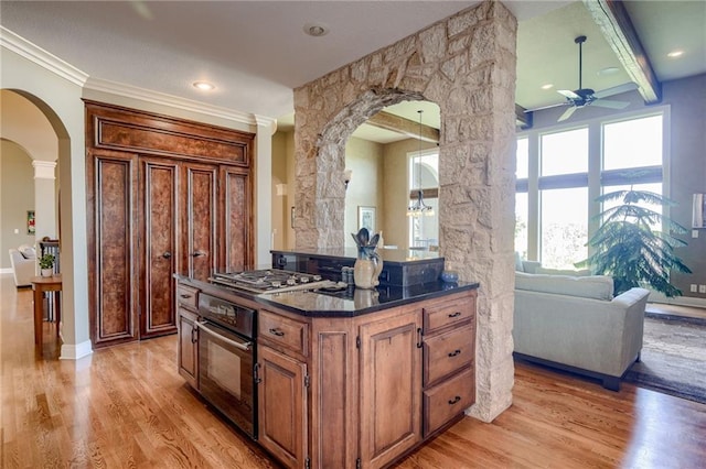 kitchen featuring black oven, stainless steel gas cooktop, dark countertops, arched walkways, and a ceiling fan
