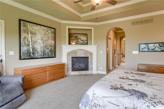 carpeted bedroom with ceiling fan, visible vents, crown molding, a tile fireplace, and a tray ceiling