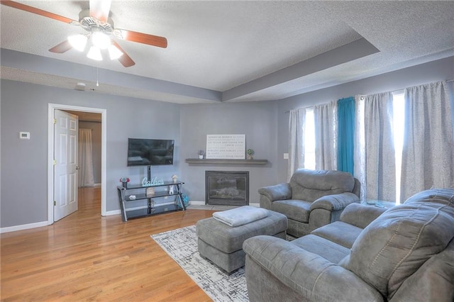 living room with a textured ceiling, baseboards, a ceiling fan, and light wood-style flooring
