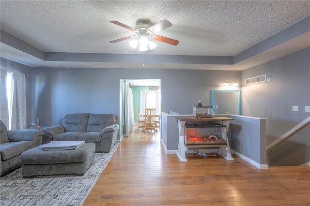 living room featuring wood-type flooring, a textured ceiling, visible vents, and plenty of natural light