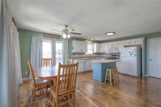 kitchen with wood finished floors, white appliances, ceiling fan, white cabinetry, and a sink