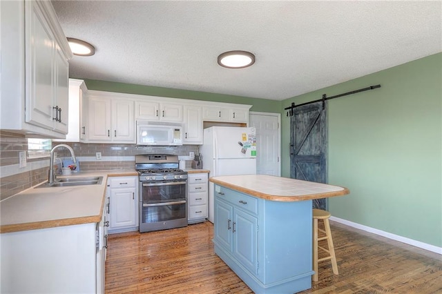 kitchen featuring decorative backsplash, a barn door, a sink, white cabinets, and white appliances