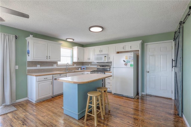 kitchen with a kitchen island, white appliances, light countertops, white cabinetry, and a sink