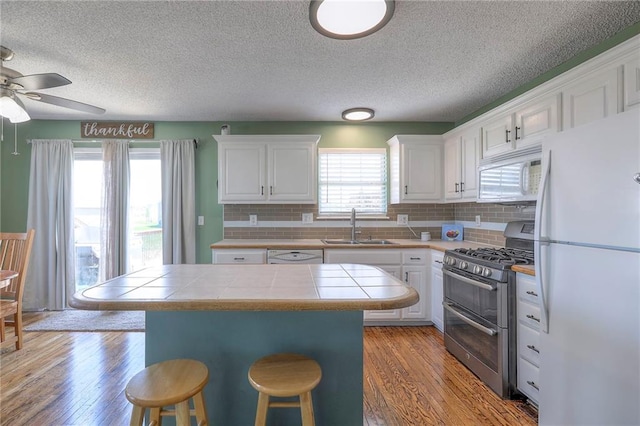 kitchen featuring a textured ceiling, a sink, white cabinets, tile counters, and white appliances