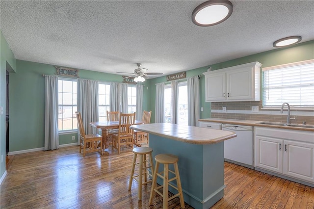 kitchen featuring wood finished floors, white dishwasher, tile counters, a textured ceiling, and a sink