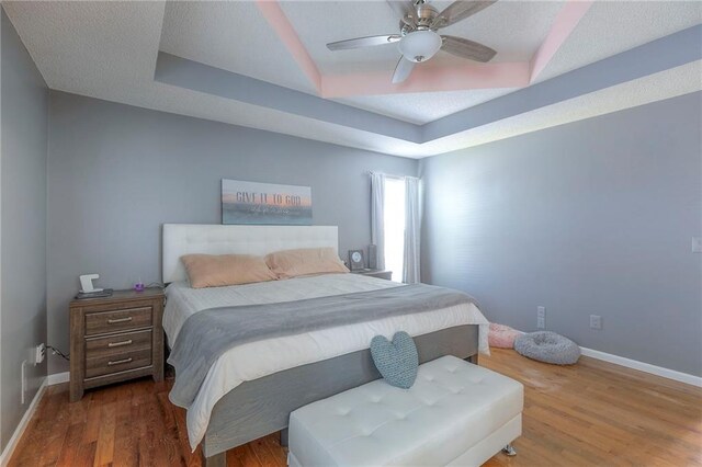bedroom with a ceiling fan, baseboards, wood finished floors, and a raised ceiling