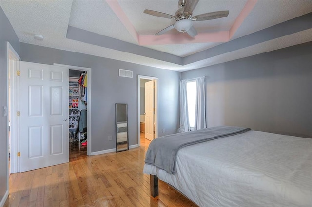 bedroom with visible vents, light wood-style floors, baseboards, a raised ceiling, and a spacious closet