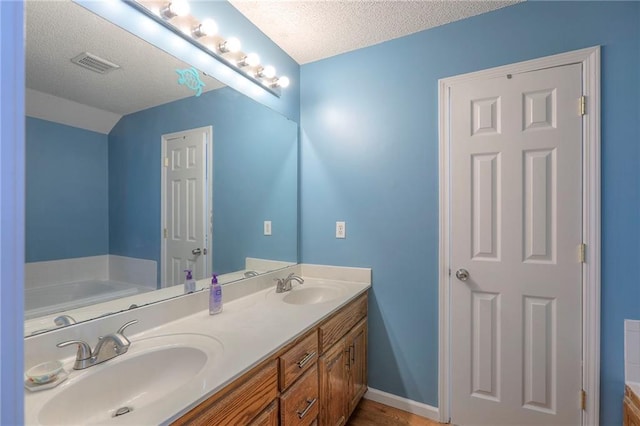 full bath with a sink, a textured ceiling, and visible vents