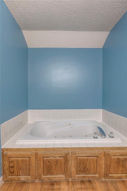 bathroom with a textured ceiling, wood finished floors, and a jetted tub