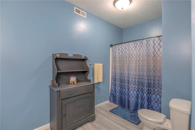 full bath featuring a shower with curtain, visible vents, wood finished floors, baseboards, and toilet