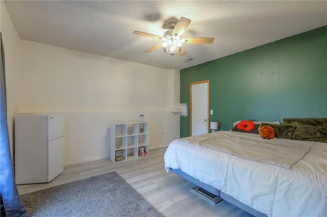 bedroom with freestanding refrigerator, a textured ceiling, ceiling fan, and light wood finished floors